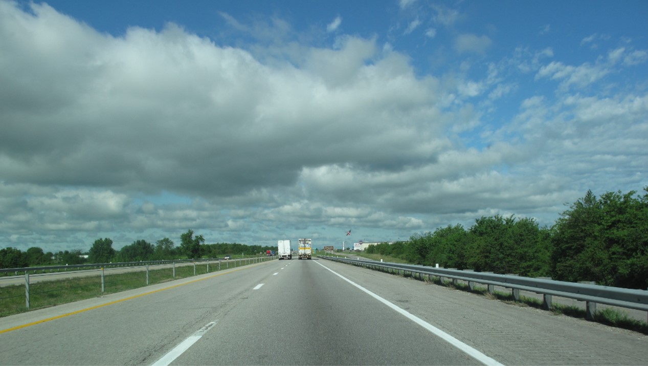 Highway image showing the back end of two tractor trailers traveling on the highway.